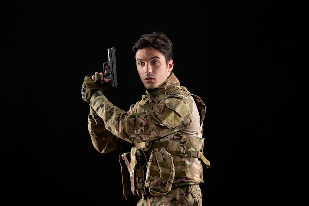 Vista frontal del militar en uniforme con pistola en pared negra