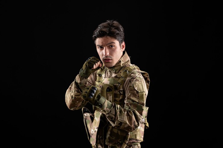 Foto gratuito vista frontal del militar en uniforme y pose de combate en la pared negra