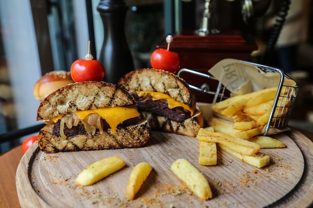 Vista frontal mitades de hamburguesas de carne con tomate y papas fritas con especias en un soporte