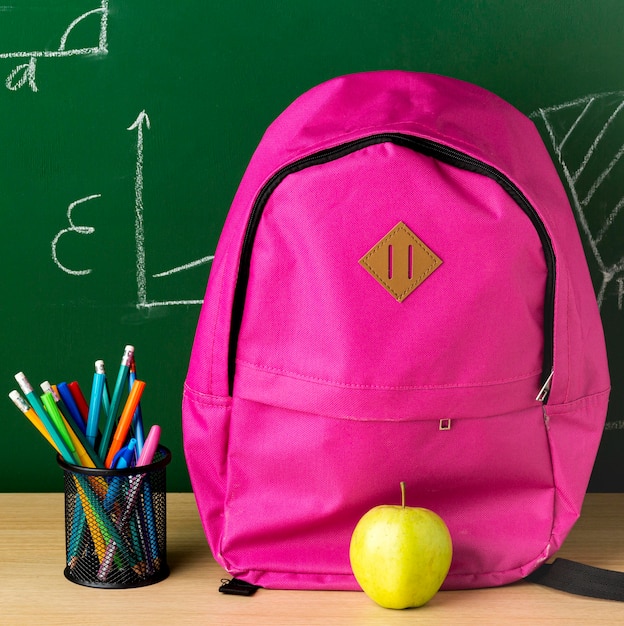 Vista frontal de la mochila para el regreso a la escuela con manzana y lápices.