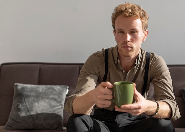 Foto gratuita vista frontal modo masculino sentado en el sofá y toma café