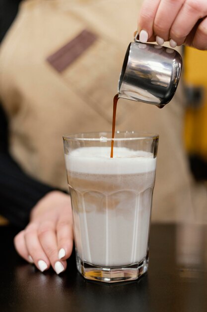 Vista frontal de la mujer barista vertiendo café en vaso de leche