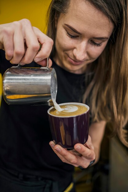 Vista frontal de la mujer barista vertiendo leche en café