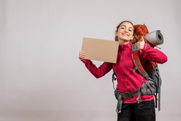 Foto gratuita vista frontal de una mujer bonita alegre con mochila grande sosteniendo cartón dando pulgares hacia arriba