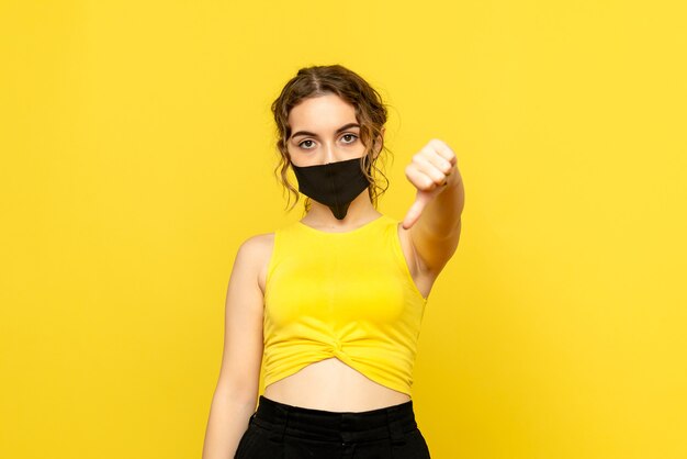 Vista frontal de la mujer bonita en máscara negra sobre amarillo