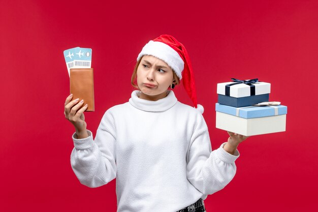 Vista frontal de una mujer bonita con regalos y entradas sobre fondo rojo.