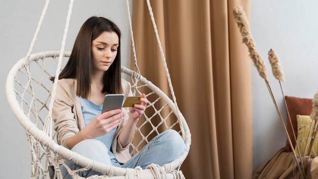 Vista frontal de la mujer en casa con teléfono inteligente y tarjeta de crédito