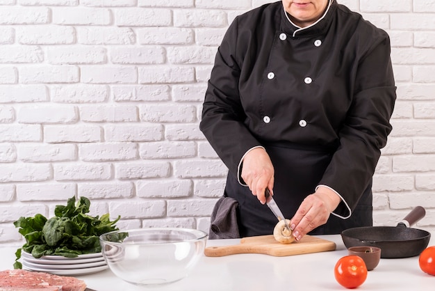 Vista frontal de la mujer chef cortar champiñones