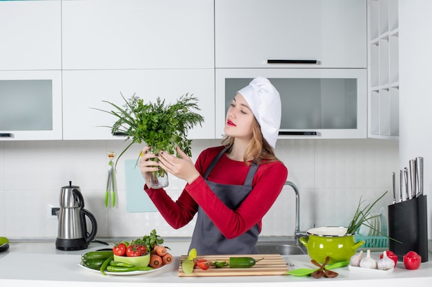 Vista frontal de la mujer chef con sombrero de cocinero sosteniendo verdes en botella