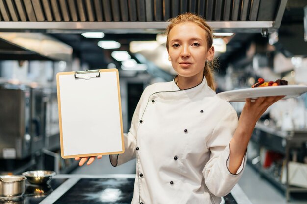Vista frontal de la mujer chef sosteniendo plato y portapapeles