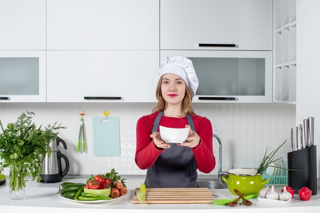 Vista frontal de la mujer chef en uniforme sosteniendo el tazón en la cocina