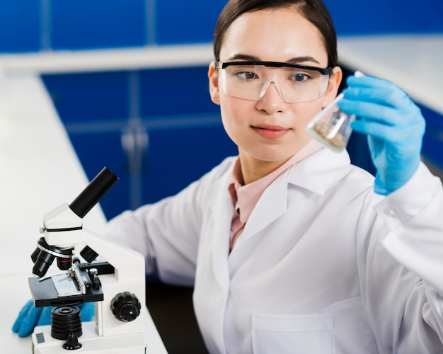Vista frontal de la mujer científica con microscopio y sustancia de laboratorio
