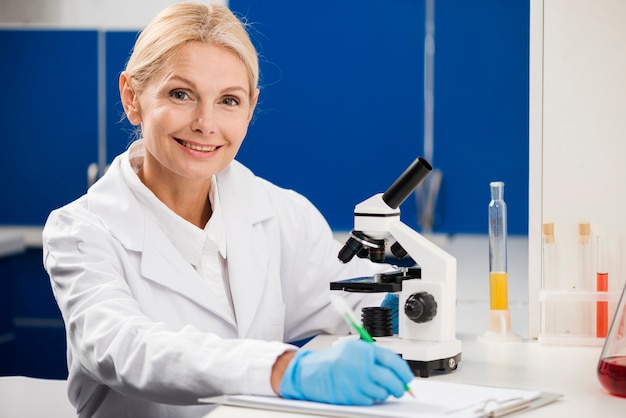 Vista frontal de la mujer científico posando con microscopio en el laboratorio