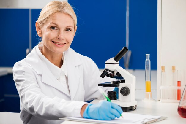 Vista frontal de la mujer científico posando con microscopio en el laboratorio