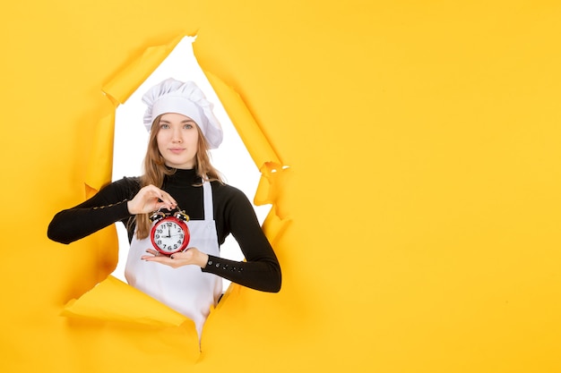 Vista frontal mujer cocinera en gorra de cocinero blanca sosteniendo el reloj en color amarillo trabajo emoción comida cocina cocina foto sol