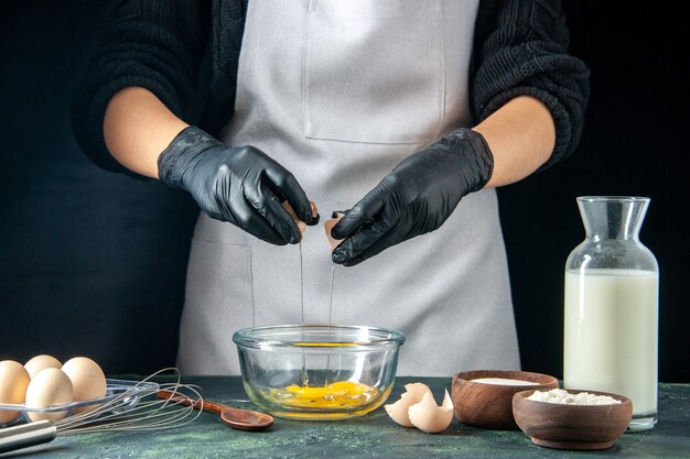 Vista frontal mujer cocinera rompiendo los huevos para la masa en pasteles oscuros pastel pastel panadería trabajador hotcake trabajo de cocina