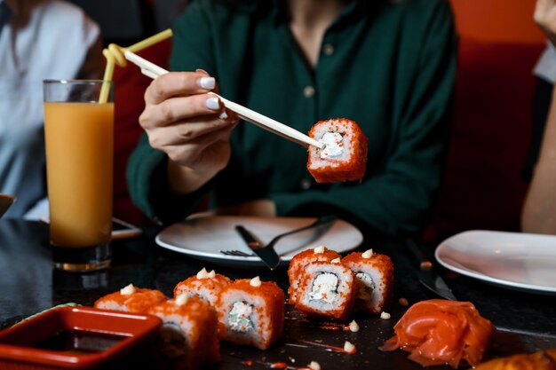 Vista frontal mujer comiendo sushi california rolls con jugo sobre la mesa