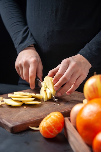 Vista frontal de la mujer cortando manzanas frescas en bandeja de madera en la mesa de la cocina