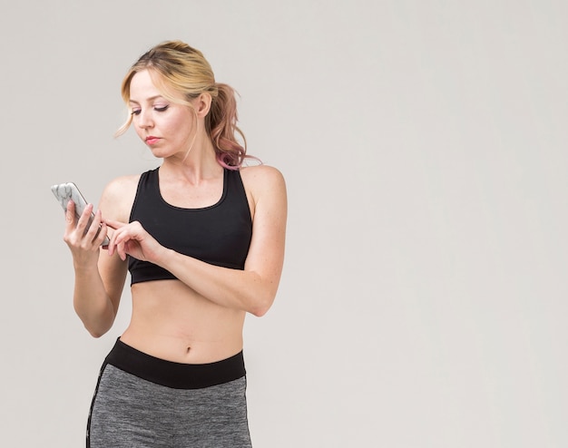 Vista frontal de la mujer deportiva mirando su teléfono inteligente