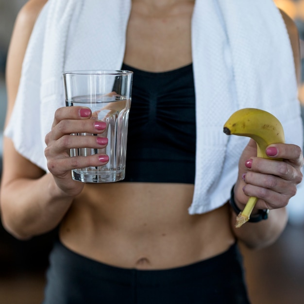 Vista frontal de la mujer deportiva con plátano y vaso de agua