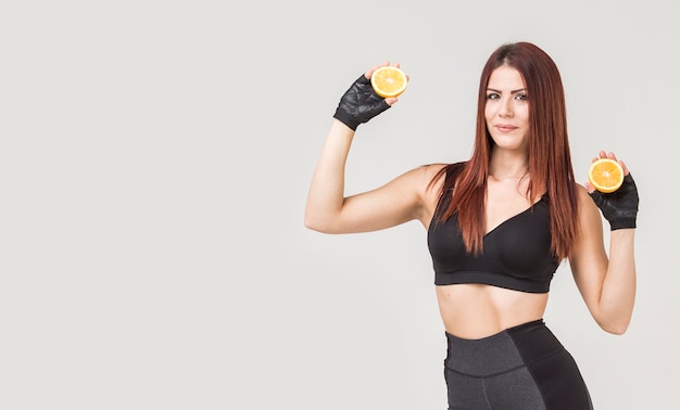 Vista frontal de la mujer deportiva posando con naranjas