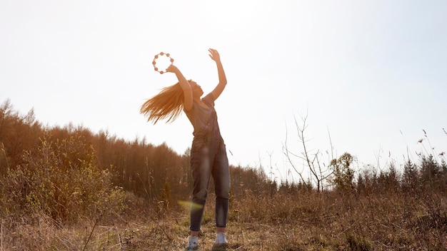 Foto gratuita vista frontal de la mujer despreocupada tocando la pandereta en la naturaleza