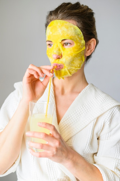 Foto gratuita vista frontal de la mujer disfrutando de una bebida mientras tiene una mascarilla