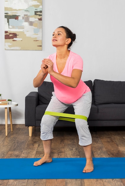 Vista frontal de la mujer embarazada en casa haciendo ejercicio con banda elástica
