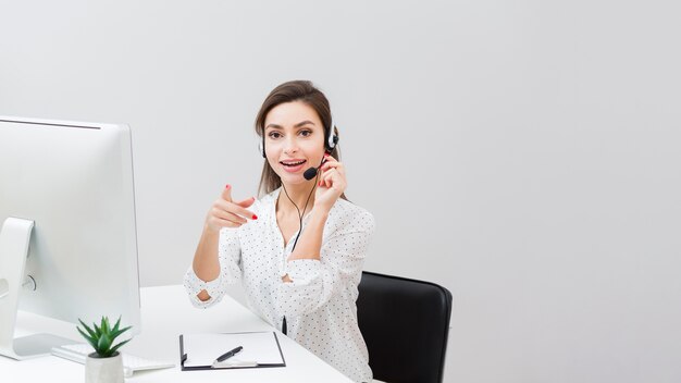 Vista frontal de la mujer en el escritorio usando auriculares y señalando