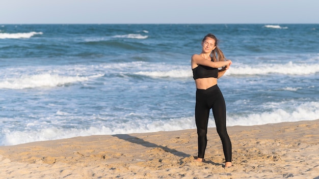 Vista frontal de la mujer estirando antes de hacer ejercicio en la playa