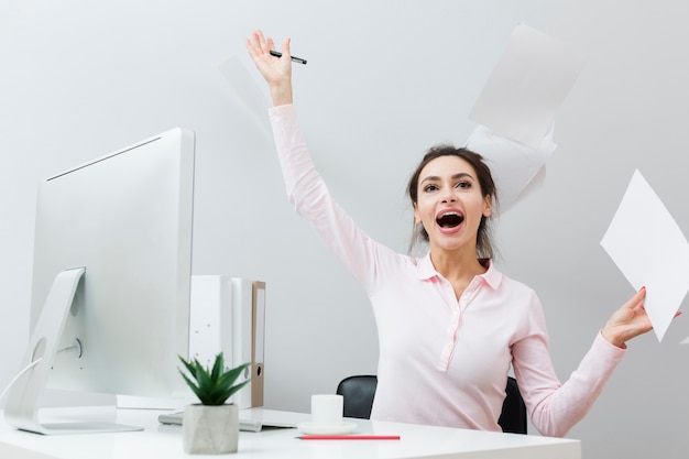 Vista frontal de la mujer extática en el trabajo tirando papeles