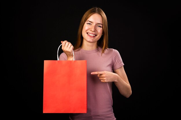 Vista frontal de una mujer feliz apuntando a su bolsa roja