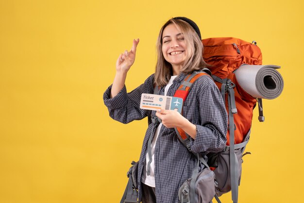 Vista frontal de la mujer feliz viajero con mochila con billete gesticulando signo de deseo