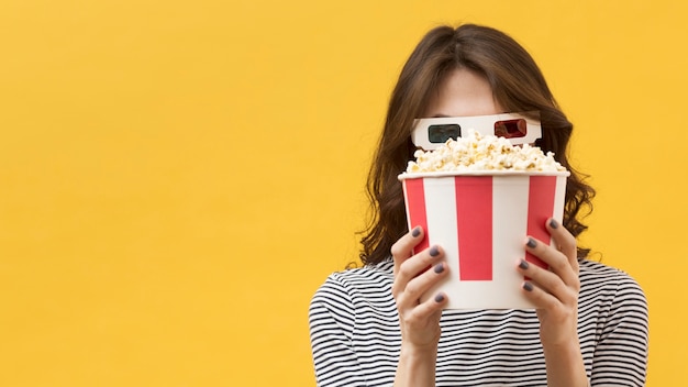 Vista frontal mujer con gafas 3d cubriendo su rostro con un cubo de palomitas de maíz