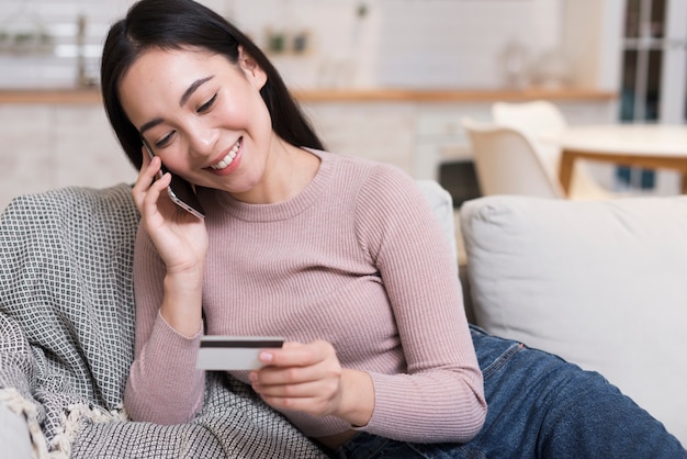 Vista frontal de la mujer hablando por teléfono mientras sostiene la tarjeta de crédito