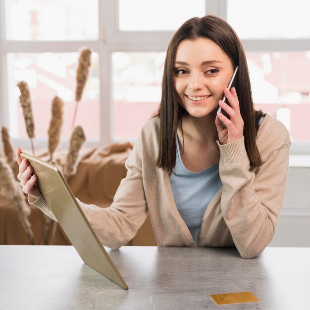 Vista frontal de la mujer hablando por teléfono y sosteniendo la tableta