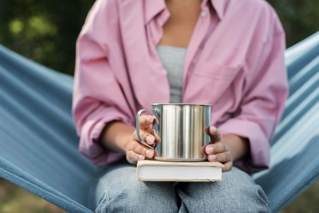 Vista frontal de la mujer en hamaca con libro y taza