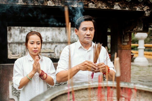Vista frontal de la mujer y el hombre rezando en el templo con incienso ardiente