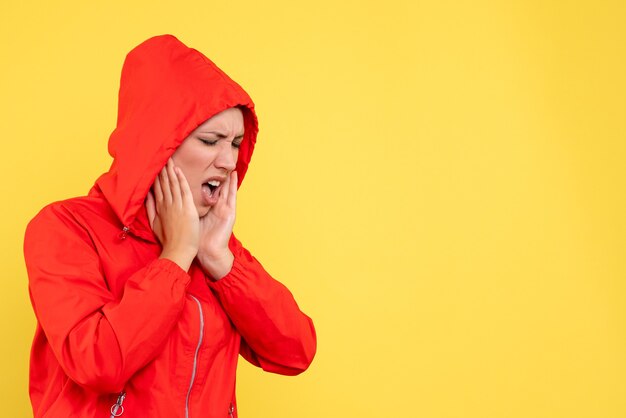 Vista frontal mujer joven en abrigo rojo con dolor de muelas sobre fondo amarillo
