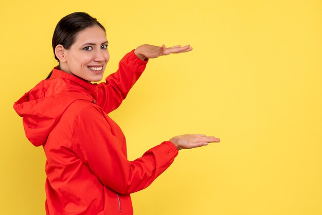 Vista frontal mujer joven en abrigo rojo sobre fondo amarillo