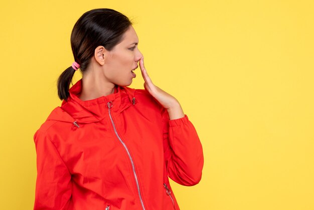 Vista frontal mujer joven en abrigo rojo sobre fondo amarillo