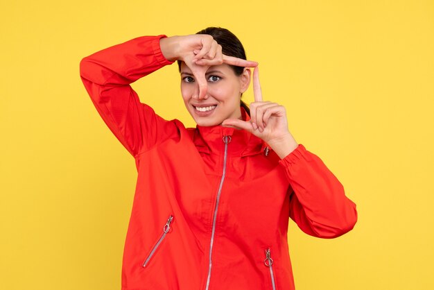 Vista frontal mujer joven en abrigo rojo sonriendo sobre fondo amarillo