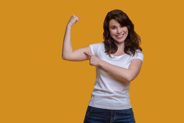 Vista frontal de una mujer joven alegre y fuerte con ropa informal que muestra su fuerza ante la cámara