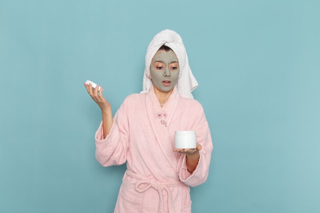 Vista frontal mujer joven en bata de baño rosa después de la ducha con crema en la pared azul baño de agua de belleza crema ducha de autocuidado baño