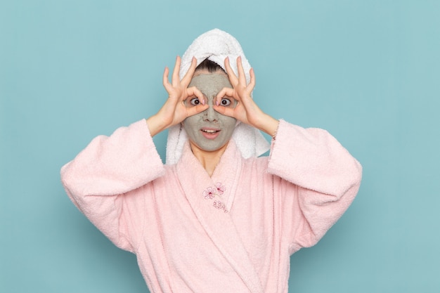 Vista frontal mujer joven en bata de baño rosa después de la ducha divertido posando en la pared azul limpieza belleza agua limpia ducha crema autocuidado