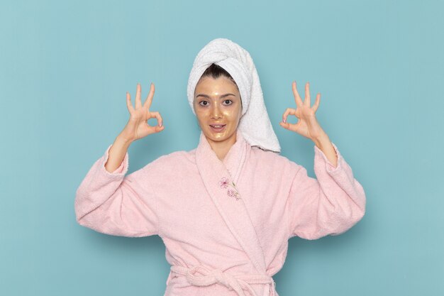 Vista frontal mujer joven en bata de baño rosa después de la ducha en la pared azul limpieza belleza agua limpia ducha crema autocuidado