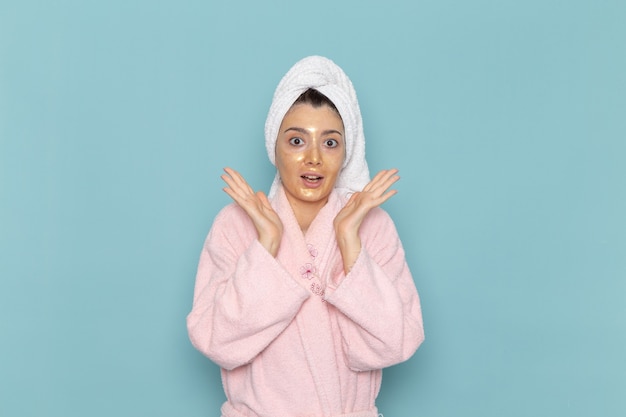 Vista frontal mujer joven en bata de baño rosa después de la ducha posando en la pared azul claro belleza agua autocuidado ducha limpia