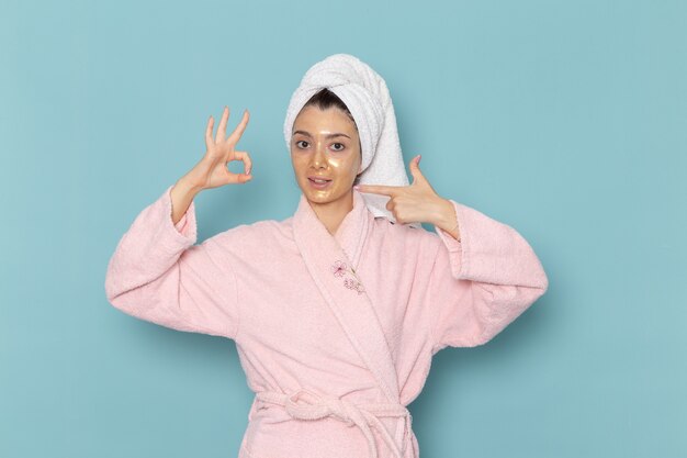 Vista frontal mujer joven en bata de baño rosa después de la ducha simplemente posando en la pared azul limpieza belleza agua limpia ducha crema autocuidado