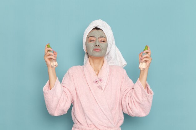 Vista frontal mujer joven en bata de baño rosa después de la ducha sosteniendo desmaquilladores en la pared azul ducha de autocuidado de crema de agua de belleza