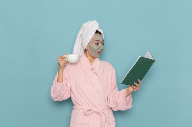 Vista frontal mujer joven en bata de baño rosa después de la ducha tomando café en la pared azul limpieza belleza agua limpia ducha de crema de cuidado personal